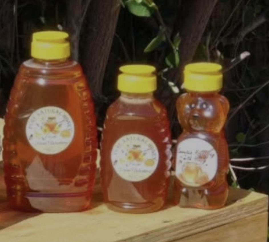Three NorCal Nectar honey bottles with yellow flip-top caps and hand-labelled fronts, photographed outdoors on a wooden board
